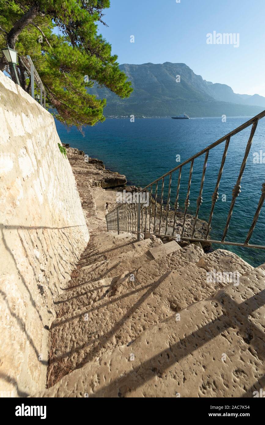 Le scale fino a rocce sull'acqua sotto le mura della città di Korcula con una vista del mare e delle montagne di Peljesac, Dalmazia, Croazia Foto Stock