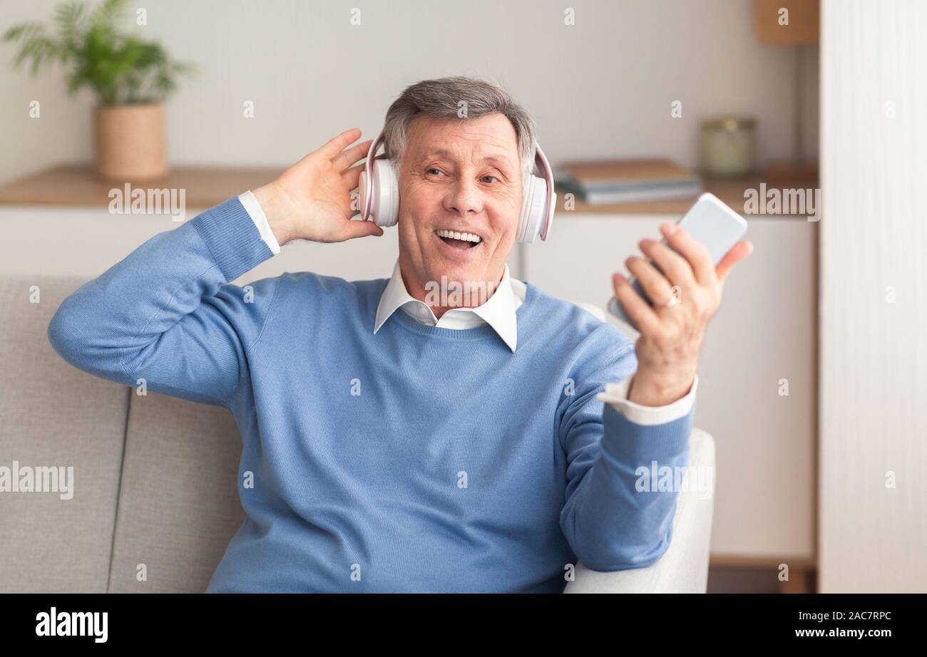 Senior uomo nelle cuffie godendo la musica seduto sul divano Indoor Foto Stock