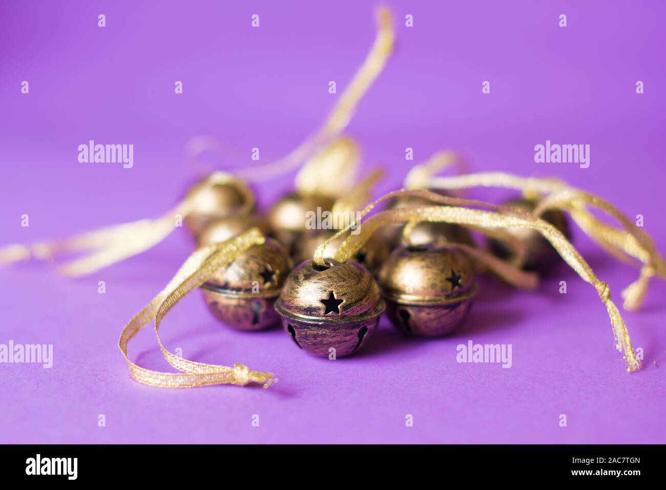 Mazzetto di ottone sleigh bells decorazioni con glitter nastri su uno sfondo violetto. Foto Stock