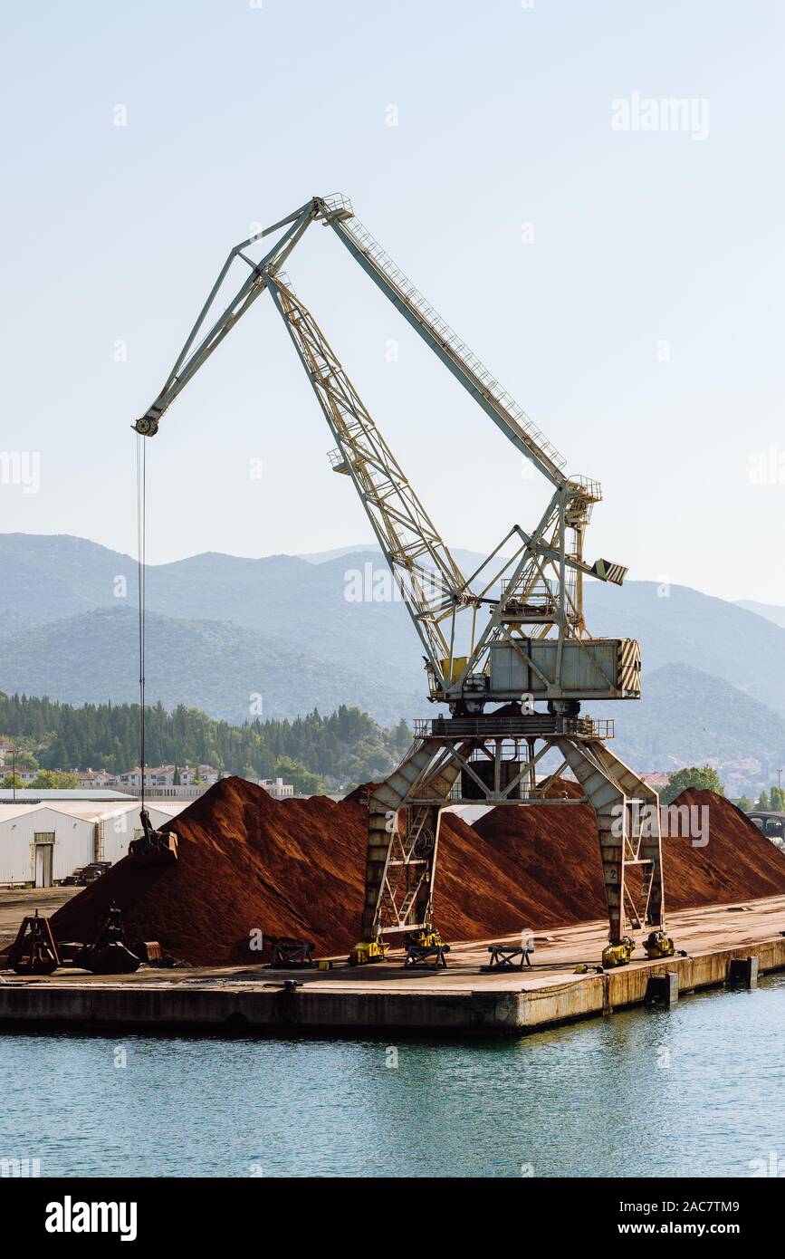 Il caricamento con gru di cucchiaia escavatore in una pila di minerale di ferro ad una banchina di carico nel porto di Ploče, Dalmazia, Croazia Foto Stock