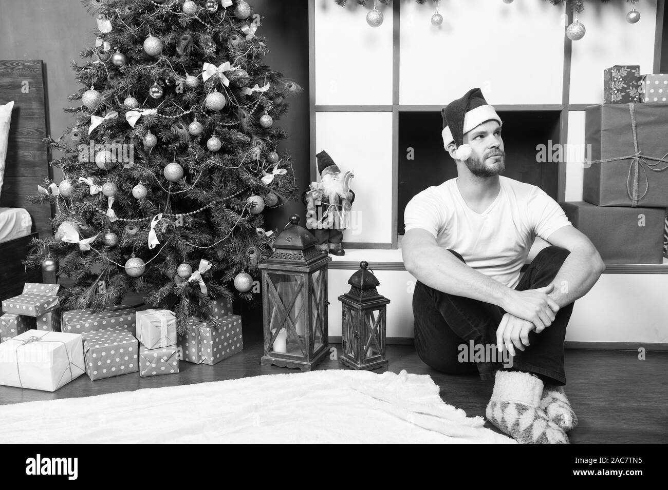 Uomo in santa hat sedersi davanti al caminetto. Macho ad albero di Natale con la presente le caselle. Natale e Anno Nuovo sala interna. Boxing day concetto. Vacanze invernali preparazione e celebrazione