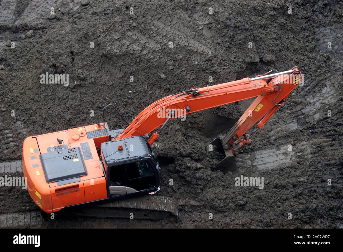 Escavatore cingolato scoop la terra con una benna, vista dall'alto. Lavori di movimento terra, di scavo su un sito in costruzione Foto Stock