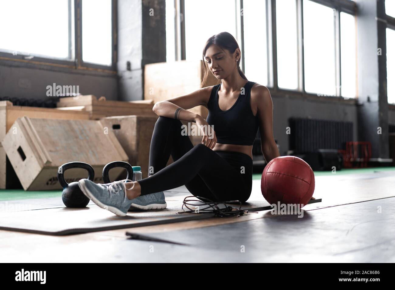 Giovane donna seduta sul pavimento dopo il suo allenamento e guardando verso il basso. Atleta femminile prendendo riposo dopo un allenamento fitness Foto Stock