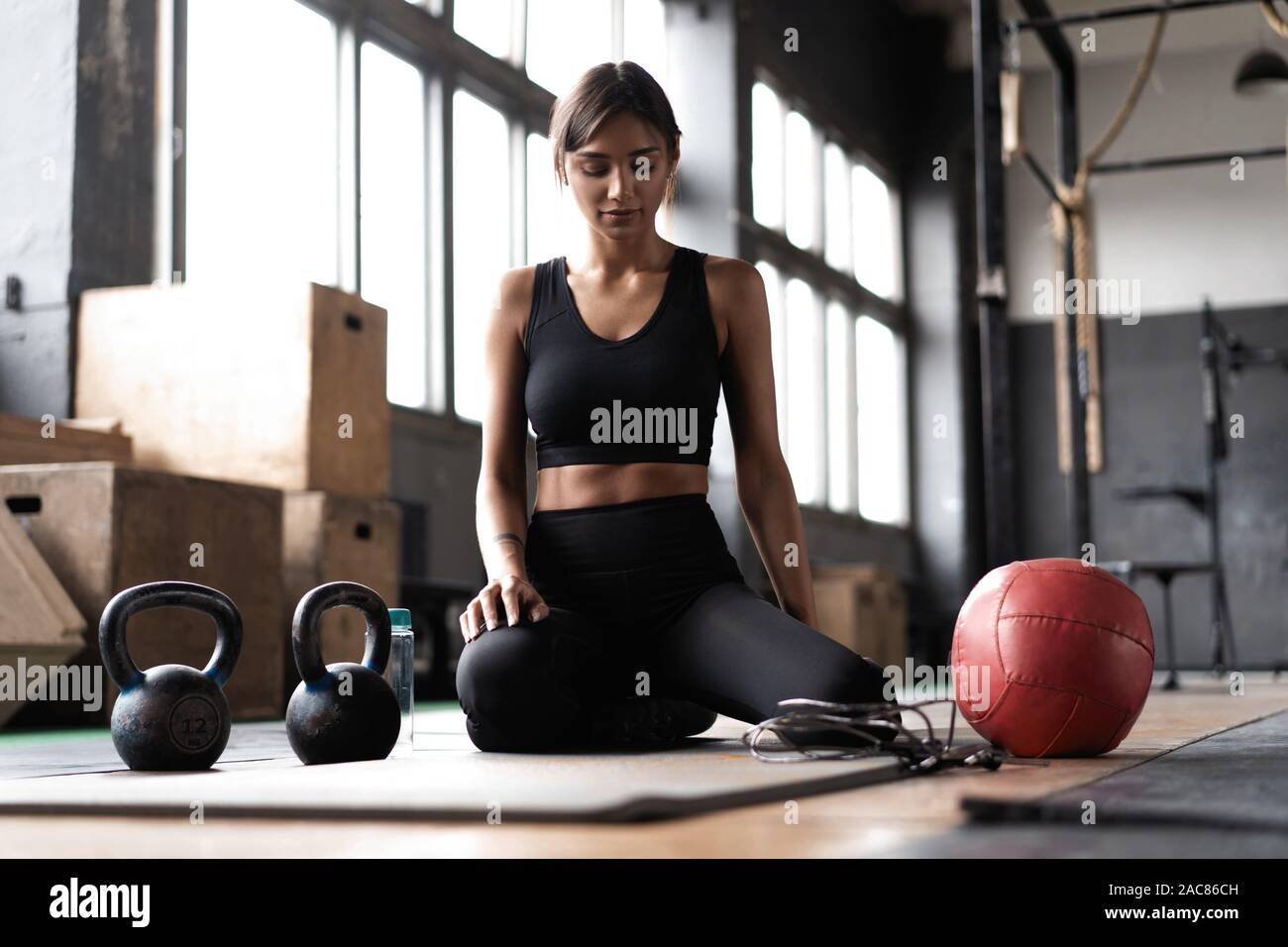 Giovane donna seduta sul pavimento dopo il suo allenamento e guardando verso il basso. Atleta femminile prendendo riposo dopo un allenamento fitness Foto Stock