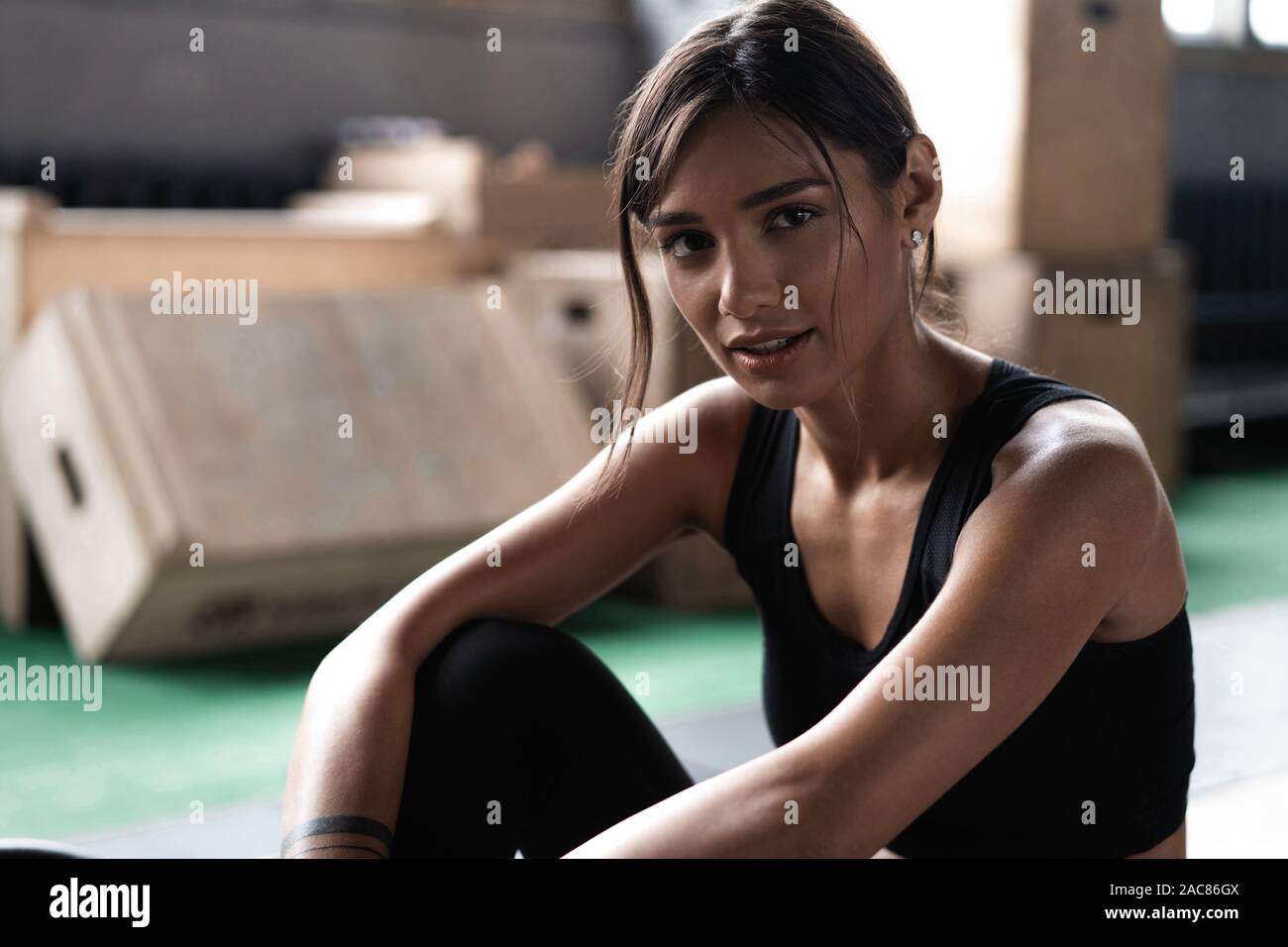 Giovane donna seduta sul pavimento dopo il suo allenamento e guardando verso il basso. Atleta femminile prendendo riposo dopo un allenamento fitness Foto Stock