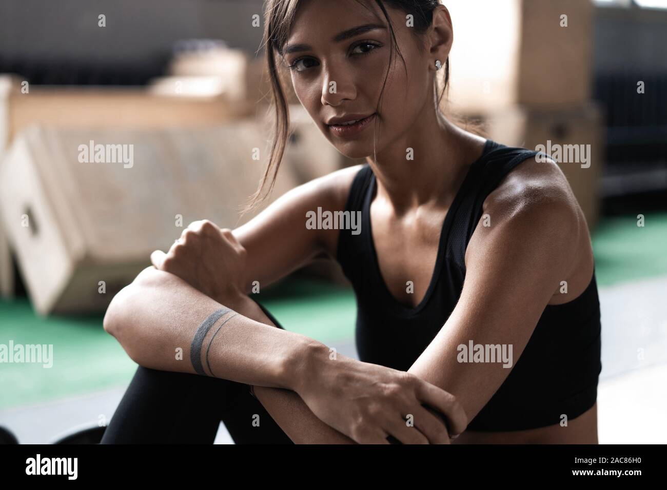 Giovane donna seduta sul pavimento dopo il suo allenamento e guardando verso il basso. Atleta femminile prendendo riposo dopo un allenamento fitness Foto Stock