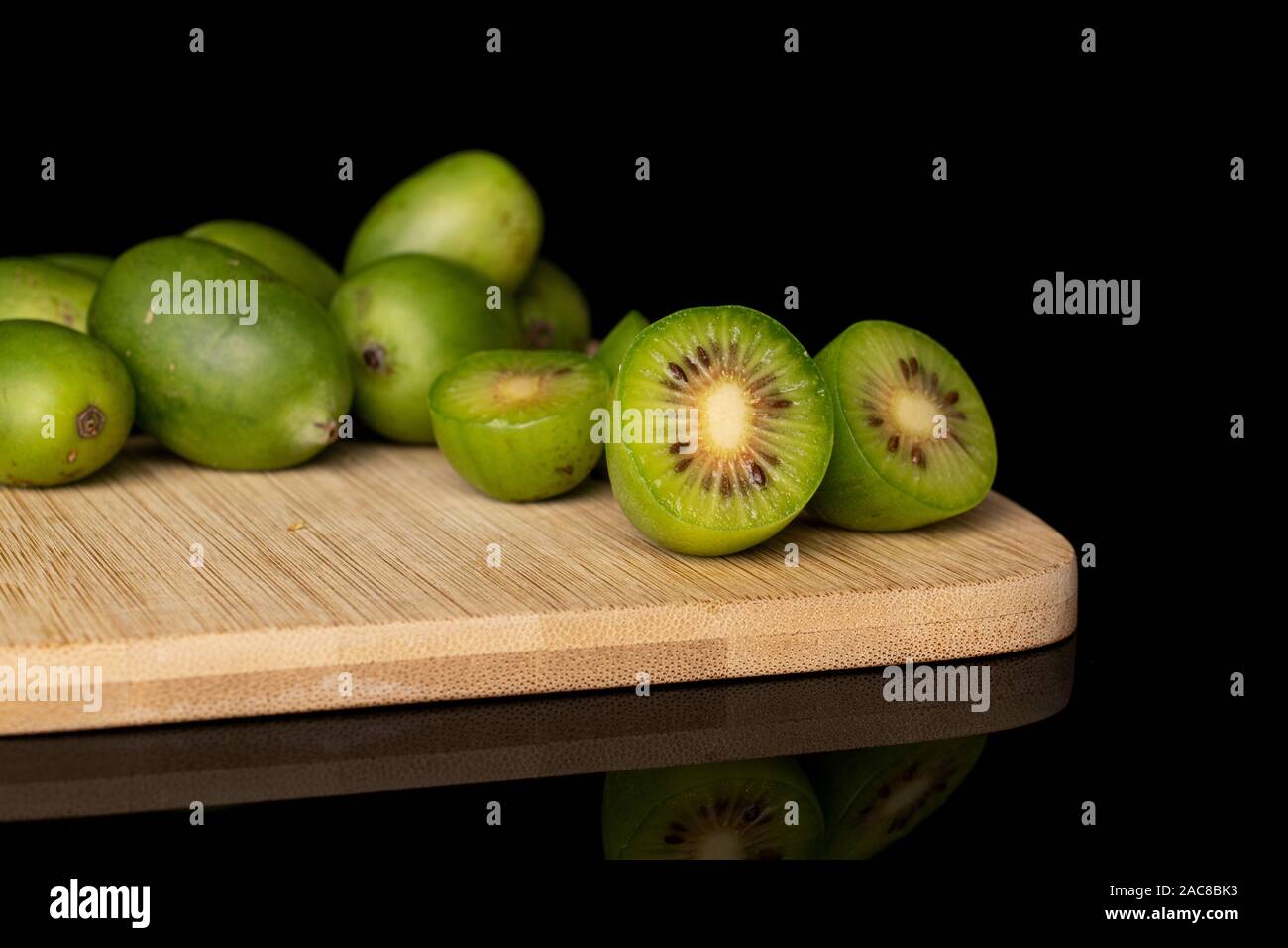 Gruppo di sacco di tutto tre metà di hardy kiwi verde sul bambù tagliere isolato sul vetro nero Foto Stock