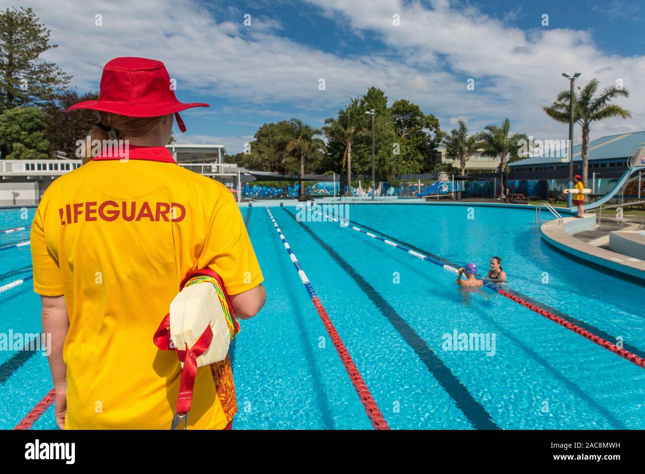 Un bagnino femmina veglia su due nuotatori in una piscina pubblica in una luminosa giornata estiva con un altro bagnino di distanza Foto Stock