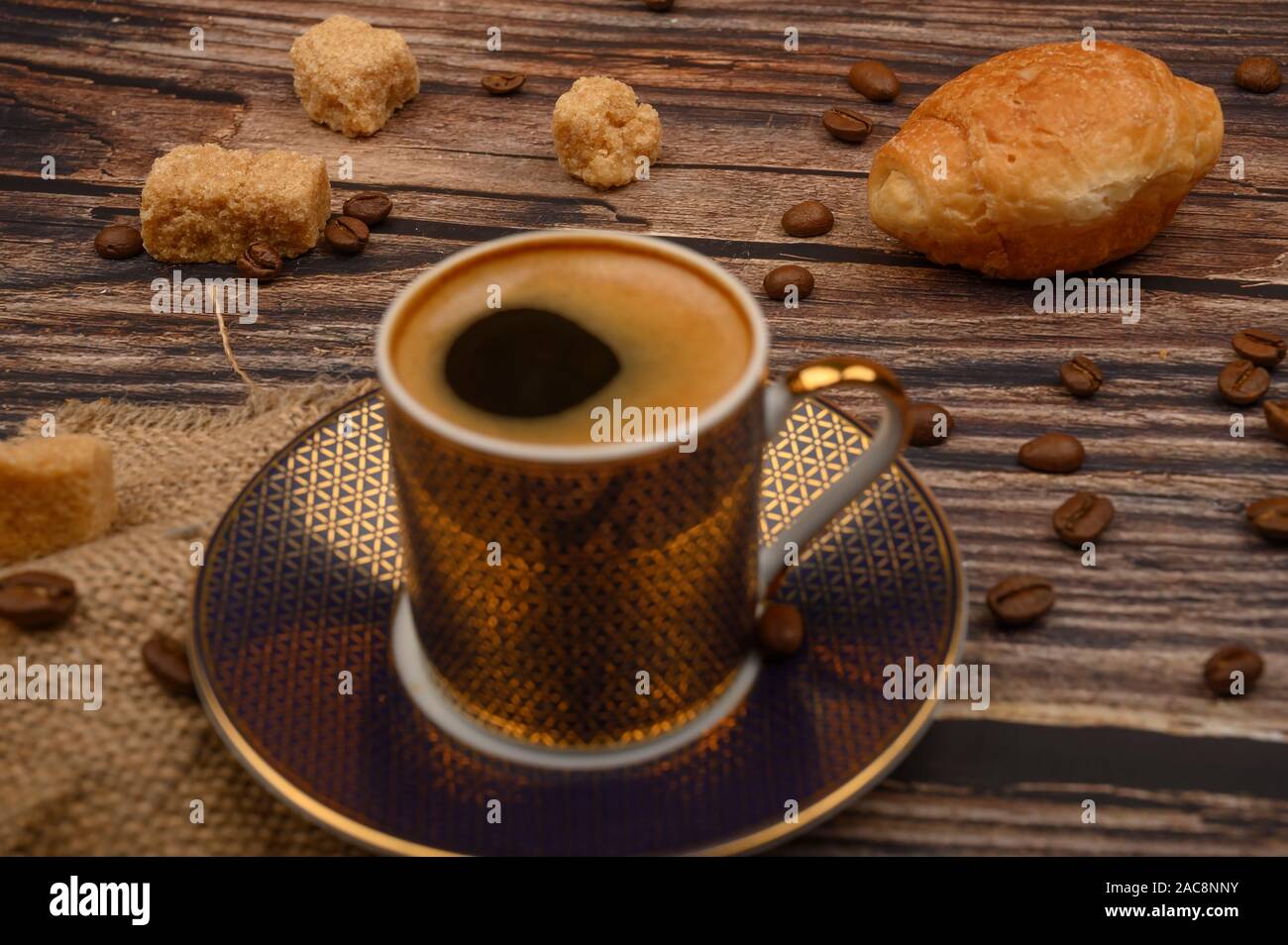 Tazza da caffè, croissant, lo zucchero di canna e i chicchi di caffè su sfondo di legno. Close up Foto Stock