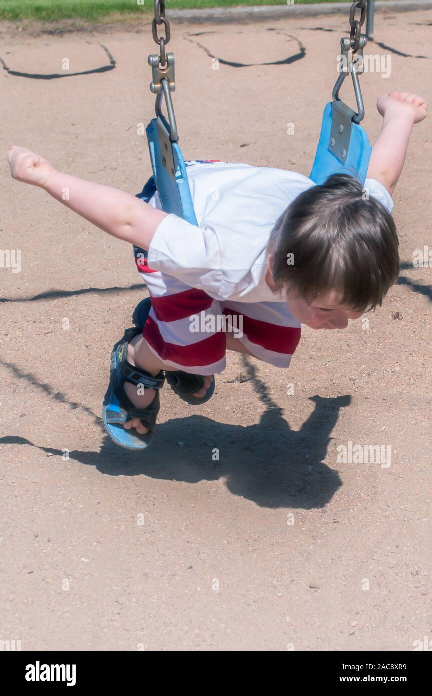Poco pre-scuola boy trascorrere la giornata giocando sulle altalene al parco della città. Foto Stock