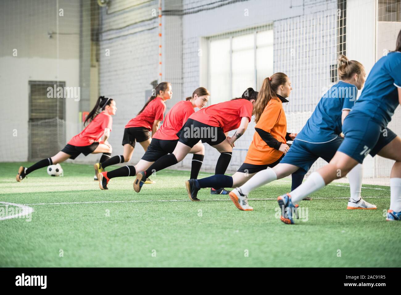 Gruppo di attivi calciatori femmina in sport uniforme di fare esercizio per stirare sul campo prima del gioco Foto Stock