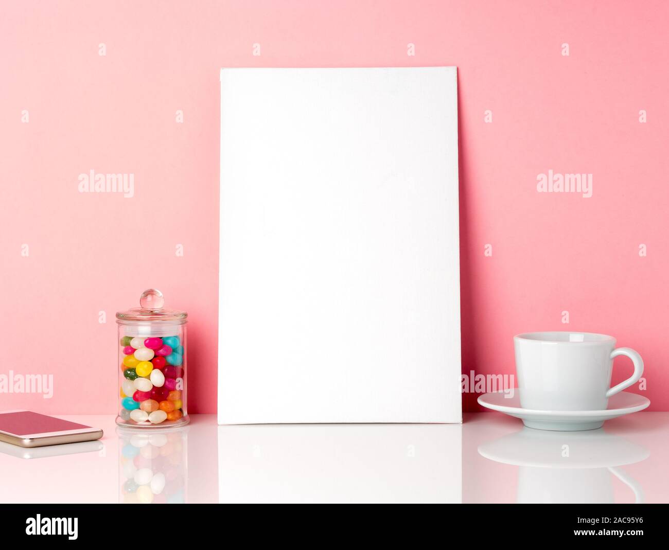 Vuoto telaio bianco e candys in vaso, una tazza di caffè o di tè su un tavolo bianco contro la parete rosa con spazio di copia Foto Stock