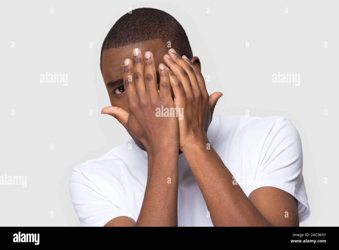Spaventata infelice African American uomo nascondersi dietro le mani, spaventato giovane maschio guardando la telecamera, sensazione di paura, stress, emozione negativa, horror mov Foto Stock