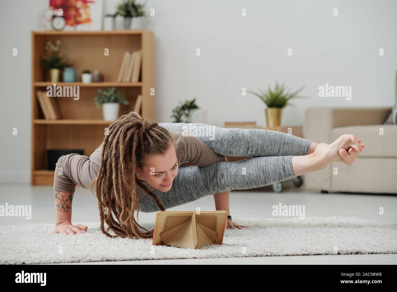 Giovane donna in piedi sulle mani in una delle posizioni di yoga nella parte anteriore del touchpad Foto Stock