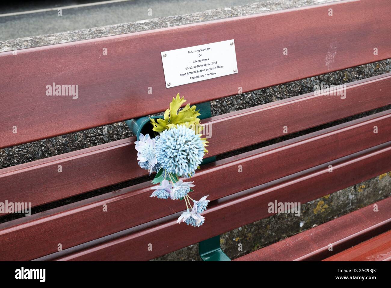 Bouquet di fiori a sinistra tra stecche di banco pubblica dedicata alla memoria di una persona cara sul lungomare. Llandudno, Galles Foto Stock