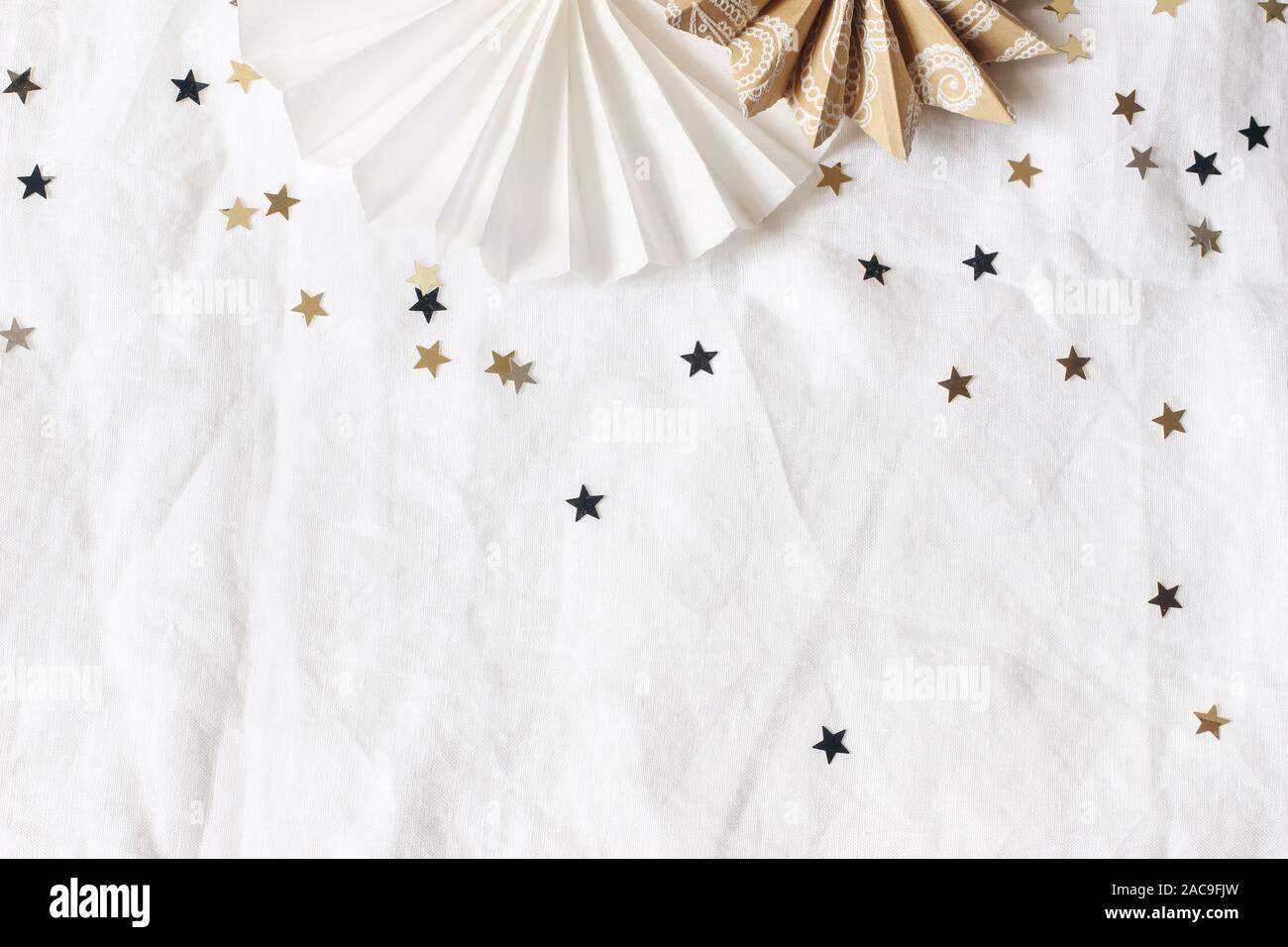 Natale e Anno Nuovo composizione. Carta decorativa di stelle, dorata e coriandoli nero su bianco lino tovaglia in background. Celebrazione, festa di compleanno Foto Stock