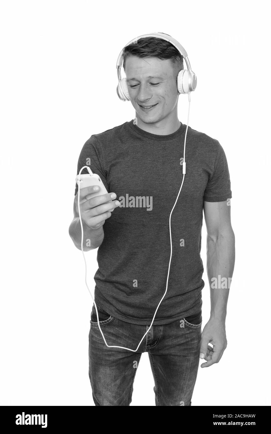 Studio shot di giovani felici uomo caucasico tenendo il telefono cellulare e ascolto di musica Foto Stock