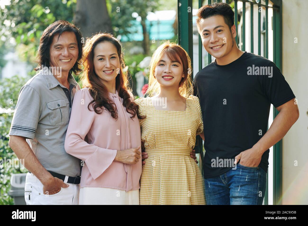 Ritratto di felice abbracciando il vietnamita i genitori e i loro figli adulti sorridente in telecamera quando in piedi all'aperto e che posano per una foto di famiglia Foto Stock