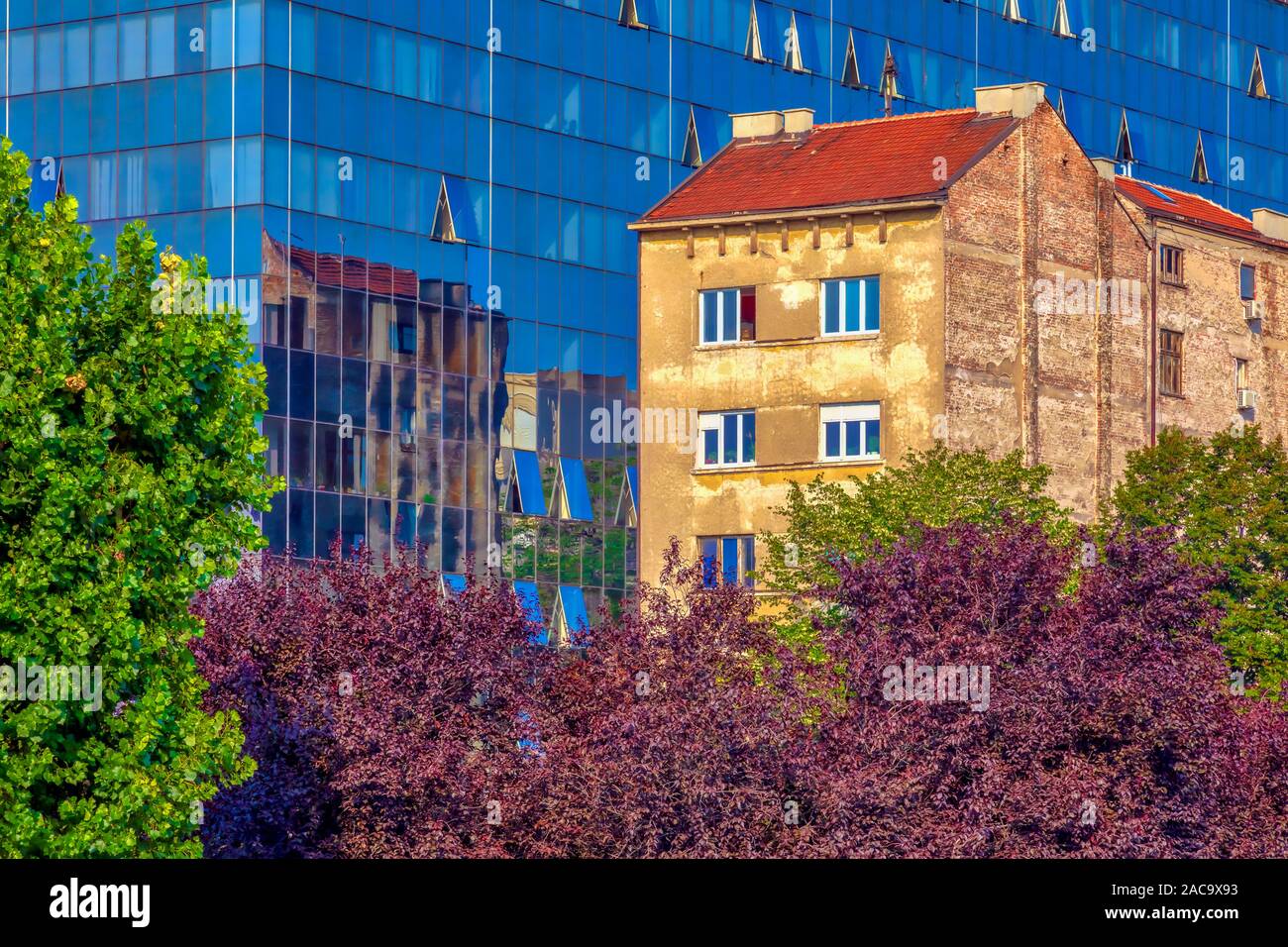 Vista di un vecchio edificio di età in piedi accanto a un nuovo e moderno con una facciata di vetro. Immagine Foto Stock