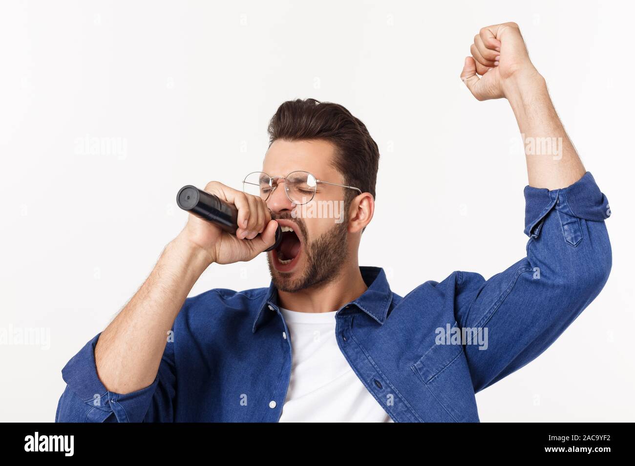 Ritratto di un entusiasta giovane uomo in t-shirt isolate su sfondo grigio, cantando. Foto Stock