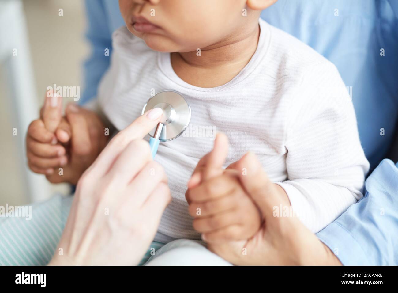 Close-up di piccolo bambino seduto sulla madre sulle sue ginocchia mentre medico esaminando lui con uno stetoscopio in ospedale Foto Stock