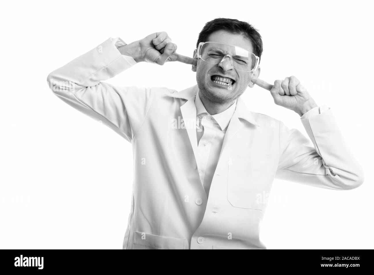 Studio shot di iracondo medico che indossa gli occhiali di protezione mentre copre le orecchie con le dita Foto Stock