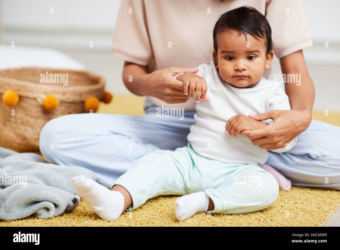 African bambino seduto sul pavimento con la madre seduta dietro di lui e tiene le mani essi trascorrere il tempo a casa Foto Stock