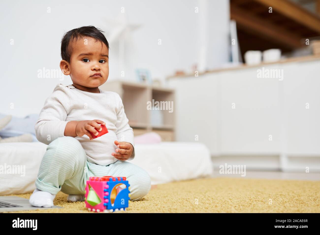 Carino il bambino africano ragazza guardando la fotocamera mentre è seduto sul pavimento e giocare con i giocattoli a casa Foto Stock