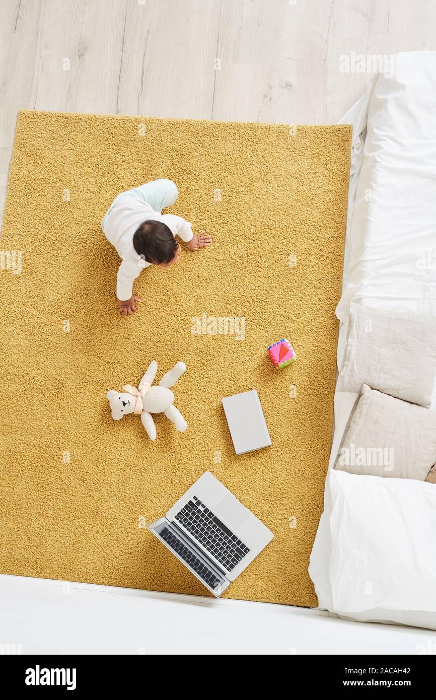 Angolo di alta vista del bambino seduto sul tappeto vicino al computer portatile e giocattoli in camera Foto Stock