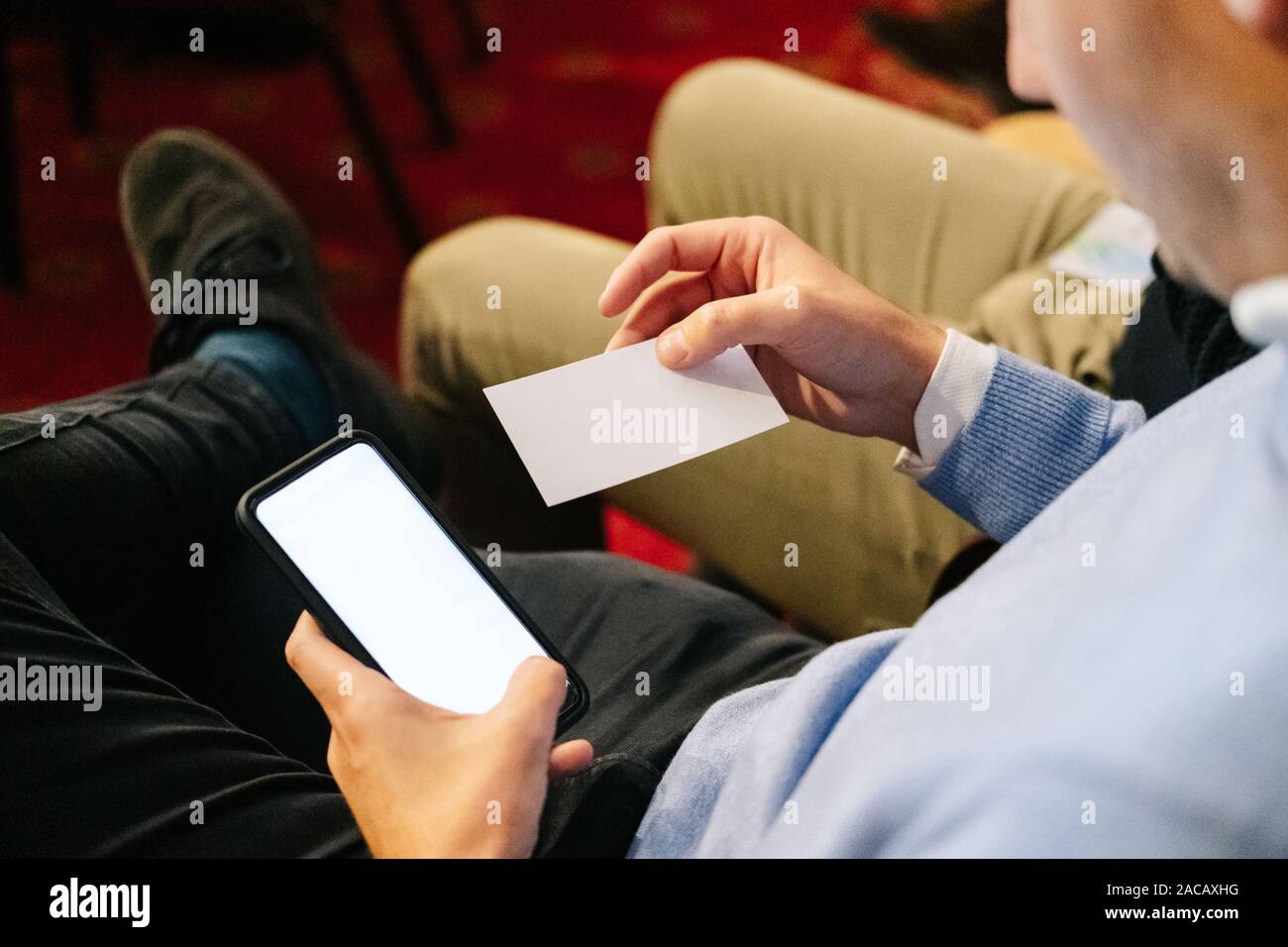 Un uomo in un incontro prende in esame una business card e utilizza il suo telefono cellulare Foto Stock