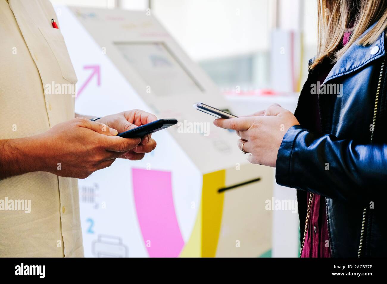 Dettaglio delle mani di un uomo e di una donna che fa uso del telefono cellulare in un congresso con un background di punto di informazione Foto Stock