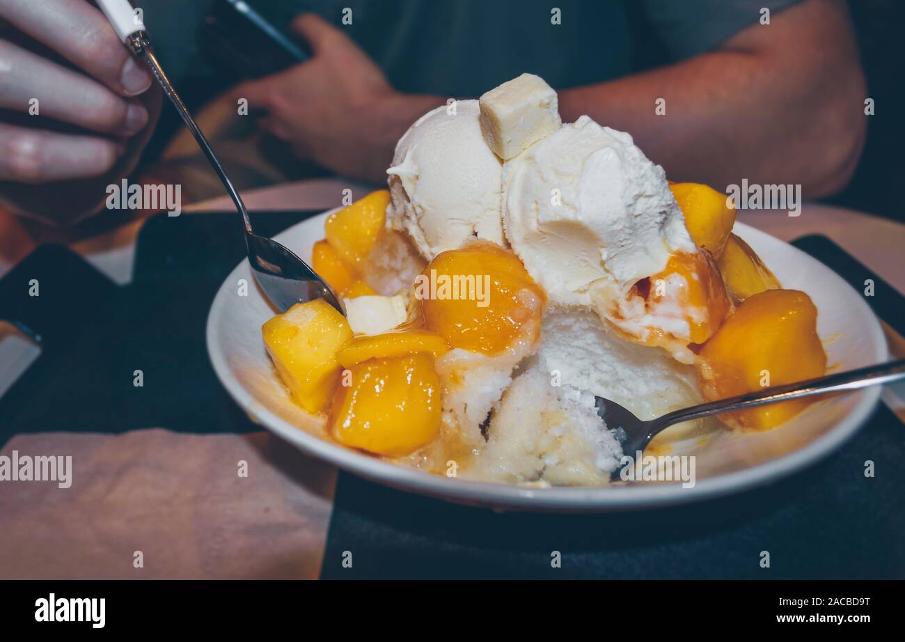 Vista ravvicinata dell uomo è mangiare freddo e mango fresco Bingsoo - coreano rasato ghiaccio con pezzi di mango e scoop di gelato Foto Stock