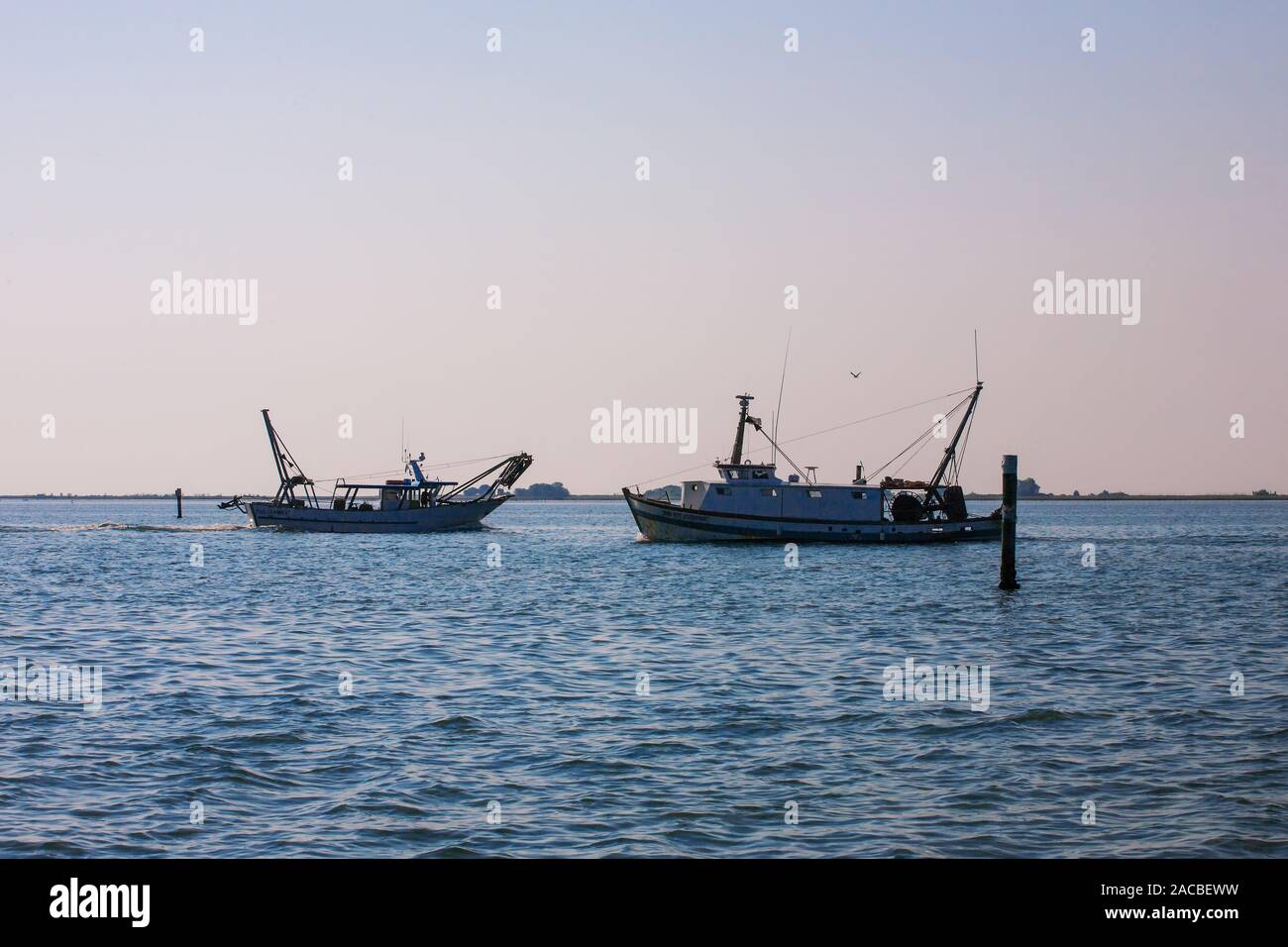 Due barche da pesca si incrociano nello stretto canale che conduce a Marano Lagunare, Laguna di Marano, Friuli Venezia Giulia, Italia Foto Stock