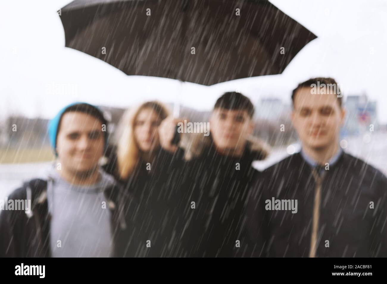 Gruppo sfocati di giovani adolescenti urbano amici sotto un unico ombrello in heavy rain - sfocare lo sfondo immagine con spazio copia - Il maltempo concept Foto Stock
