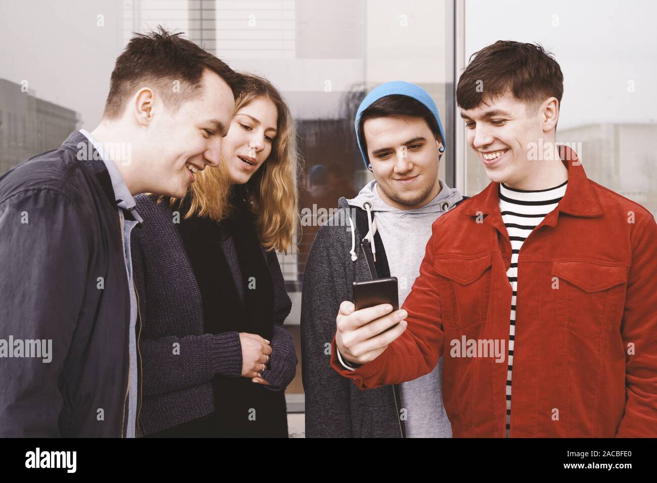 Giovane uomo che mostra qualcosa di divertente sul suo smart phone a un gruppo di amici - urban adolescenti divertendosi e ridere insieme Foto Stock