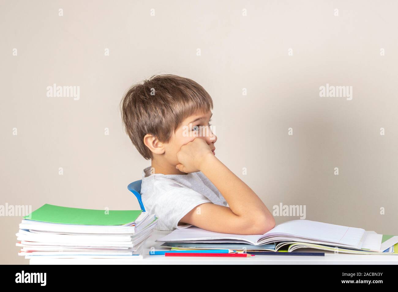 Triste stanco bambino seduto vicino a pila di notebook e di libri e di pensiero Foto Stock