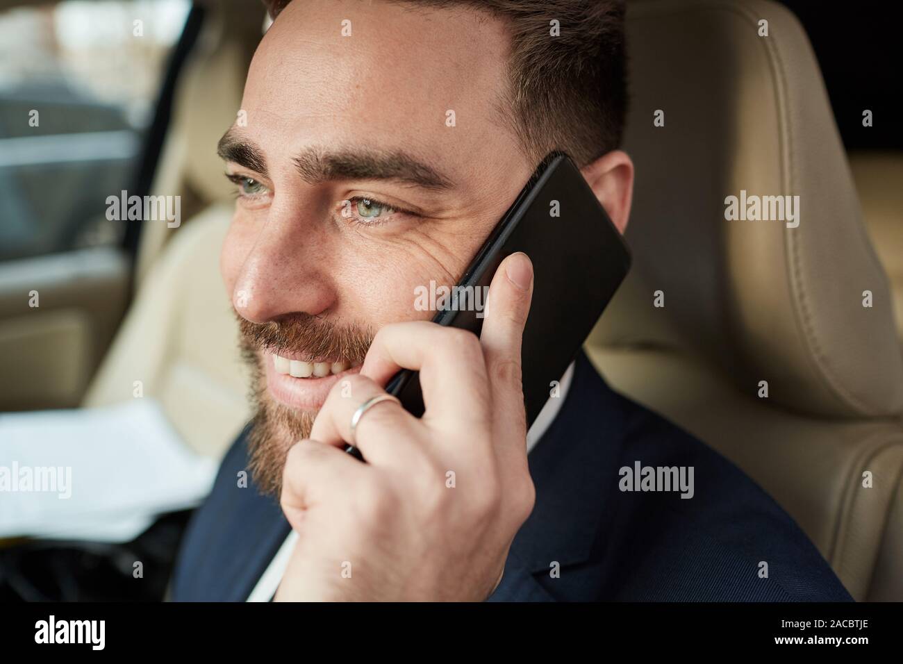 Giovani happy businessman ha una chiamata telefonica durante la guida egli parla e sorridente Foto Stock