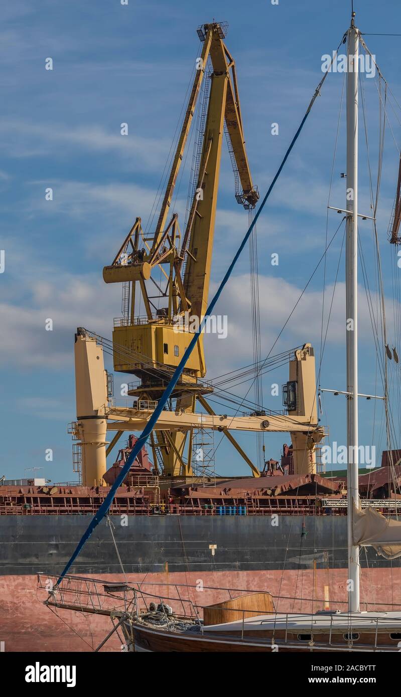 Gru industriali. Grandi gru gialle con barca a vela nella parte anteriore della foto e il cielo con le nuvole in background. Immagine di stock. Foto Stock