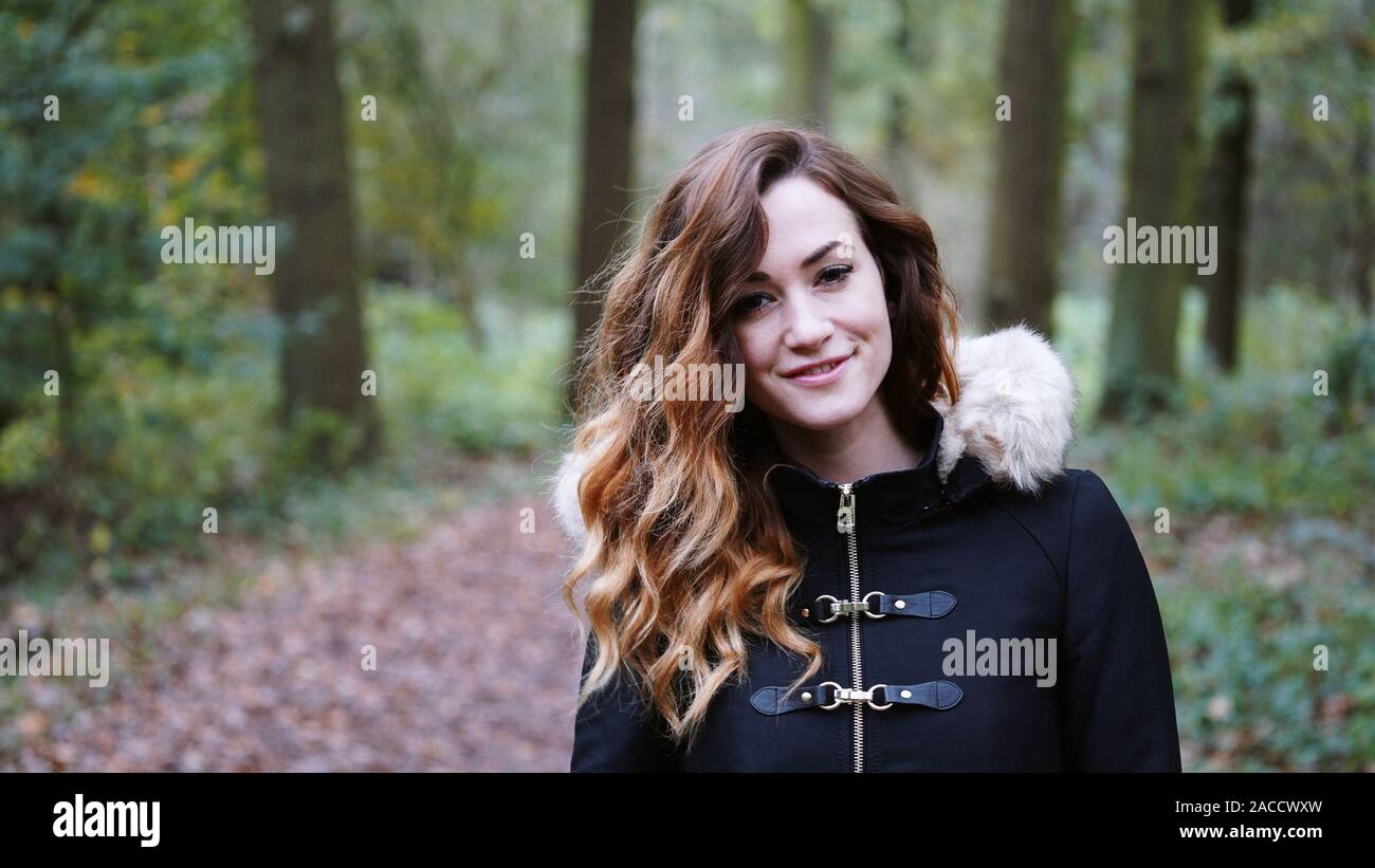 Felice giovane donna indossa cappotto invernale di andare a fare una passeggiata nel bosco in un freddo giorno di autunno Foto Stock
