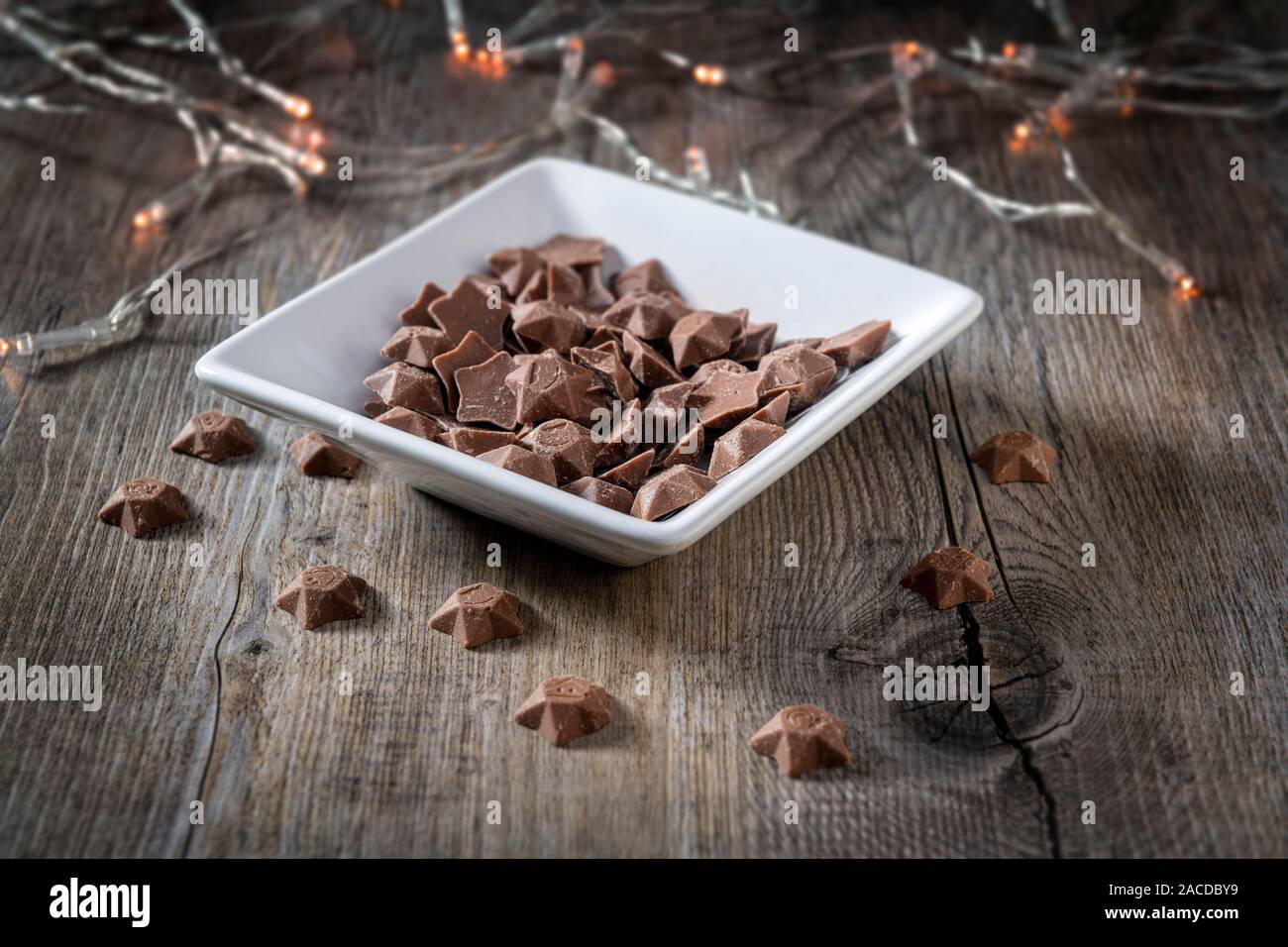 Ciotola di stelle di cioccolato su un tavolo di legno con le luci fairy Foto Stock