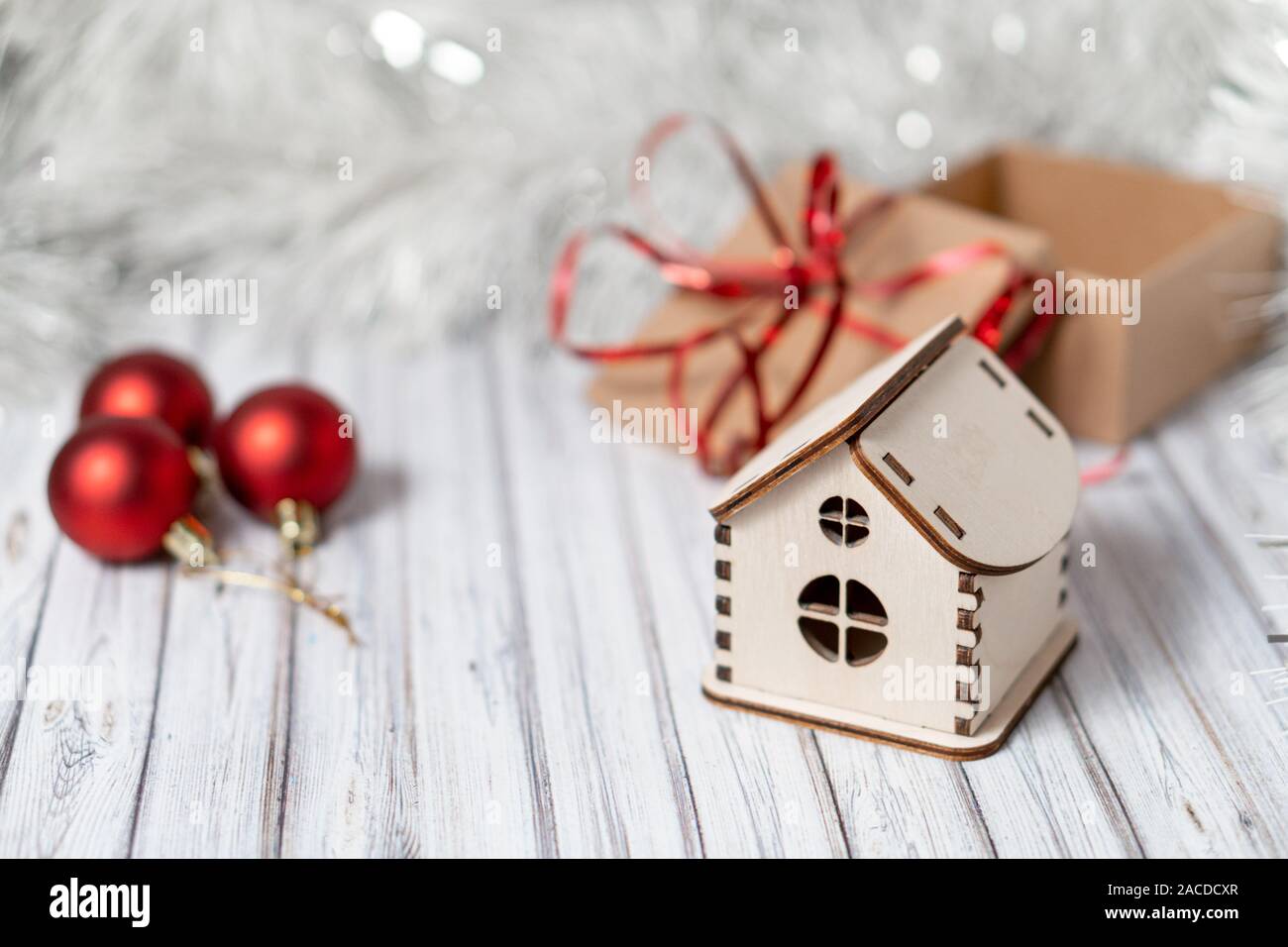 Toy casa in legno su un tavolo di legno decorato con una ghirlanda di fiori e di rosso le palle di Natale per il Nuovo Anno o XMAS Foto Stock