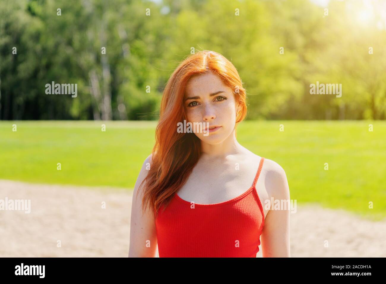 Giovane donna indossa red strappy top all'aperto in un parco su un luminoso giorno di estate Foto Stock