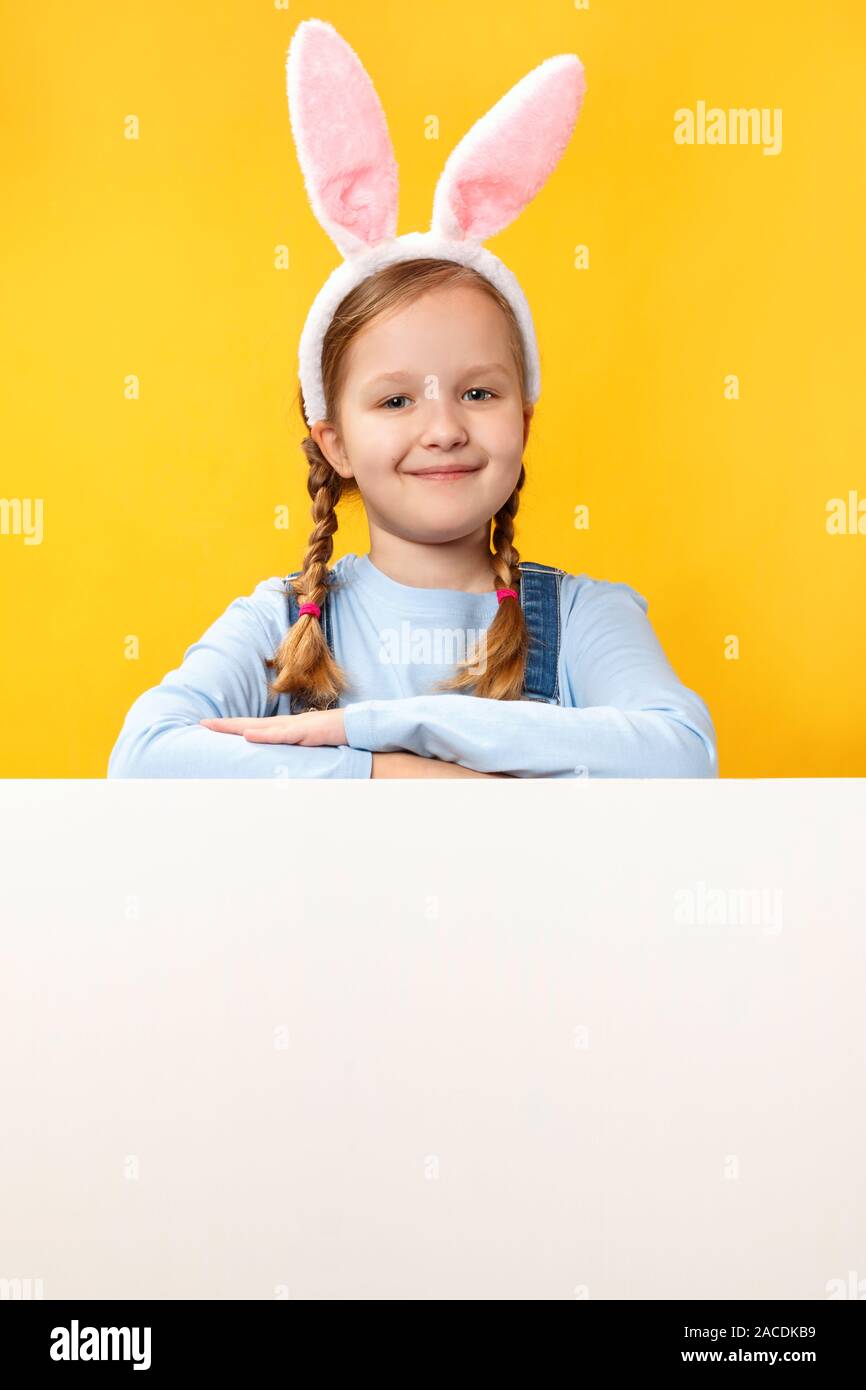 Bambino felice nelle orecchie di coniglio tenendo un vuoto spazio banner su uno sfondo giallo. Scheda di pasqua. Foto Stock