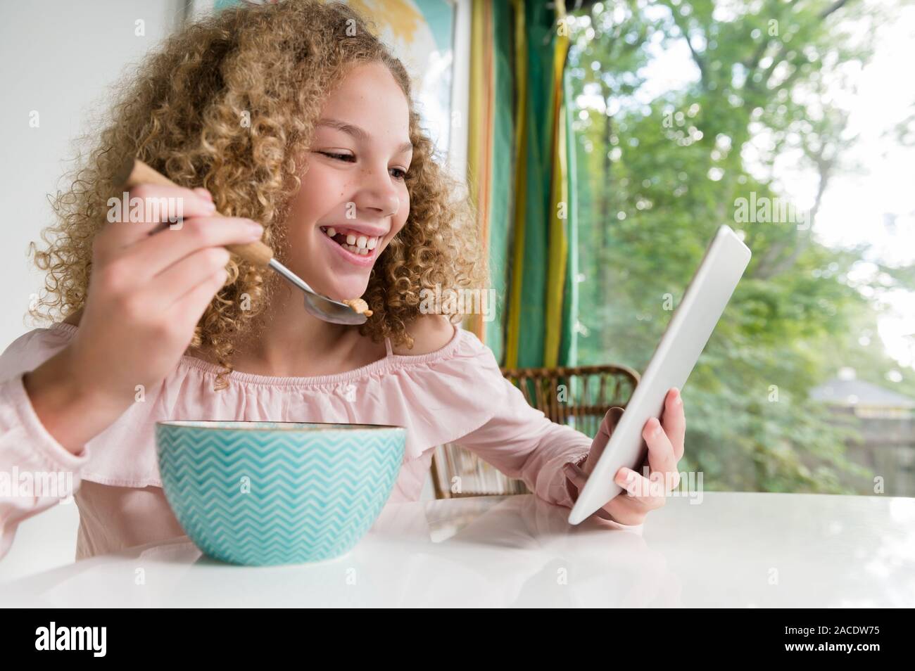 Sorridente ragazza che mangia la colazione utilizzando un tablet Foto Stock