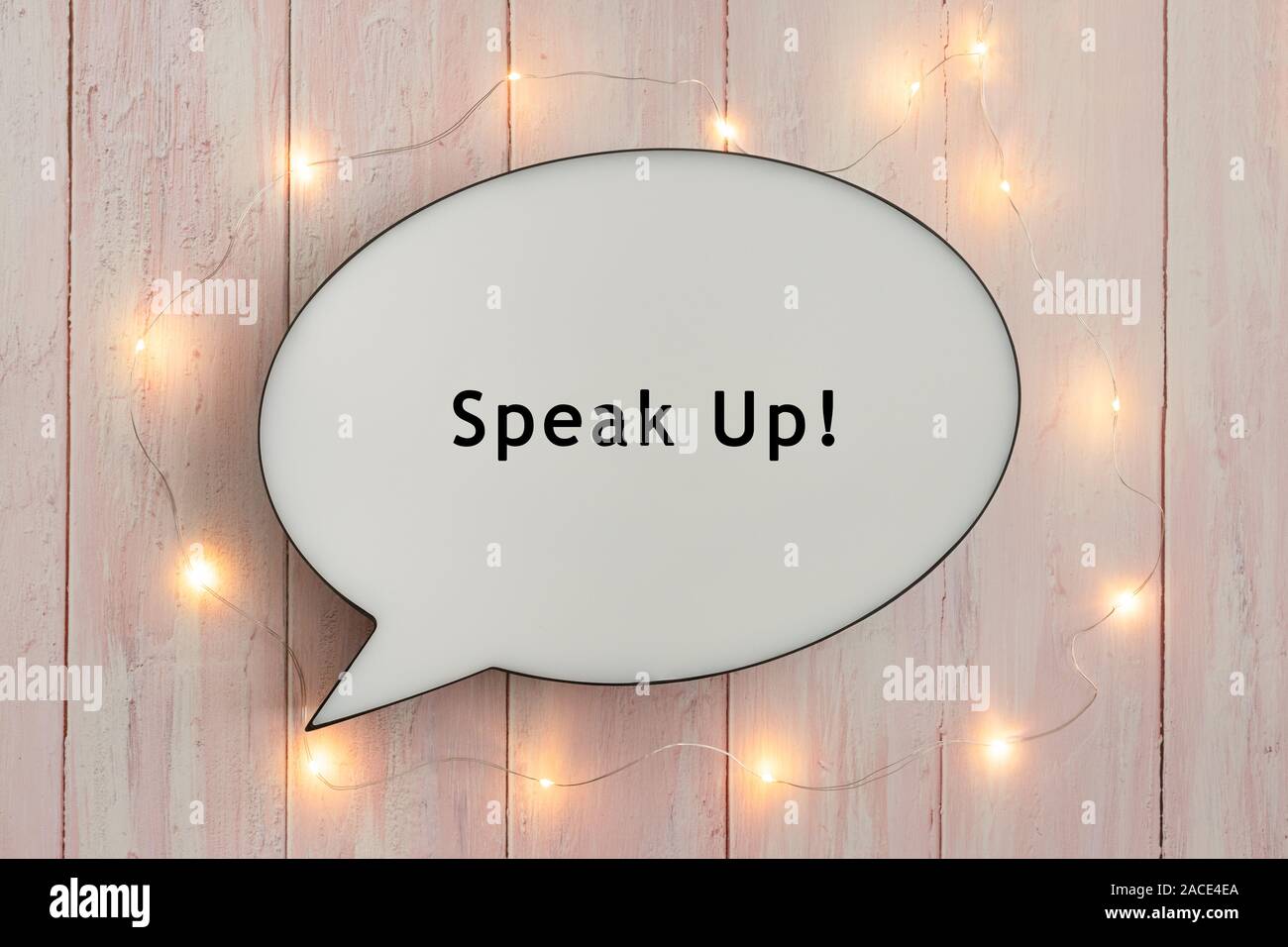 Speak Up scritto il discorso bolla, circondato da luci brillanti sul rosa sullo sfondo di legno Foto Stock