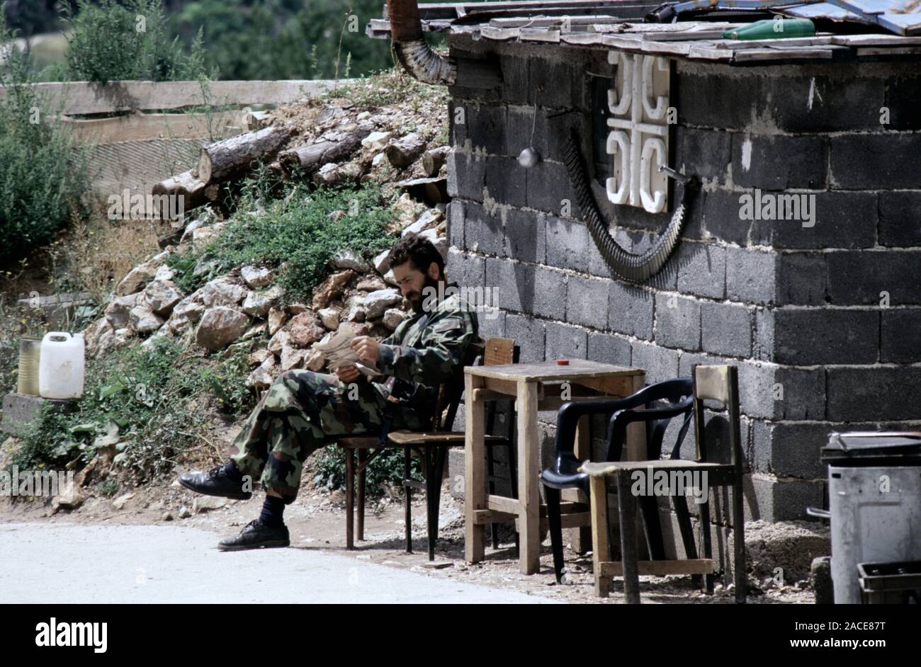 11 agosto 1993 durante l'assedio di Sarajevo: un soldato Bosnian-Serb rilassa fuori del suo bunker sul Monte Trebevic, al di sopra di Sarajevo. Una cinghia di trascorso M2 Browning .50 cartucce calibro appendere al di sotto di un serbo simbolo a croce sulla parte anteriore della capanna. Foto Stock