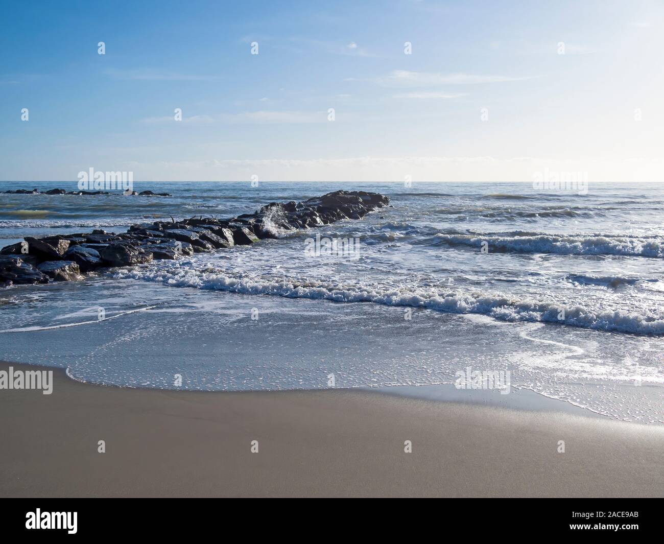 Spiaggia di sabbia con le onde che si infrangono e molo roccioso. Mare Mediterraneo, l'Europa. Foto Stock