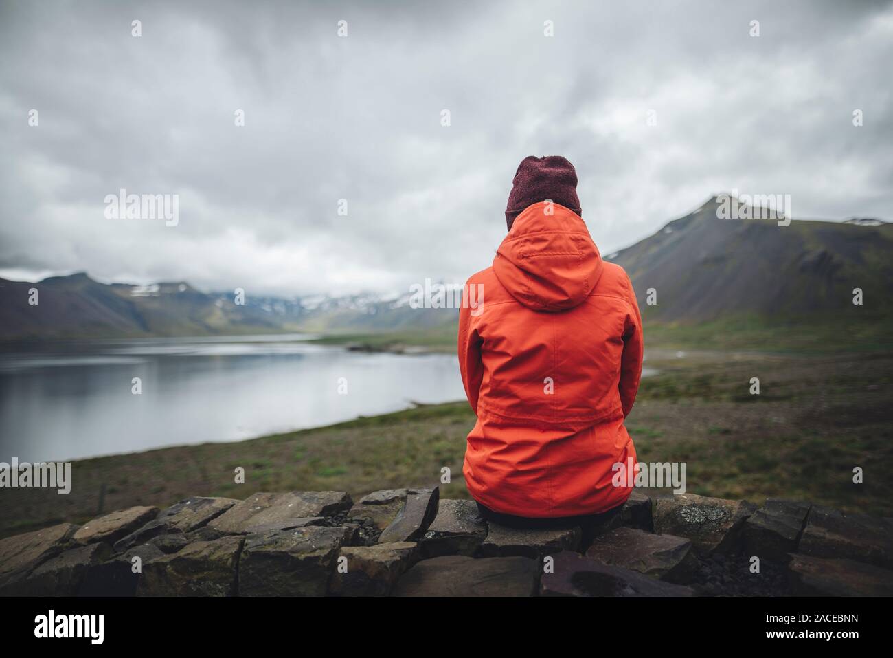 Donna che indossa un impermeabile rosso seduta dal fiordo a Snufellsnes, Islanda Foto Stock