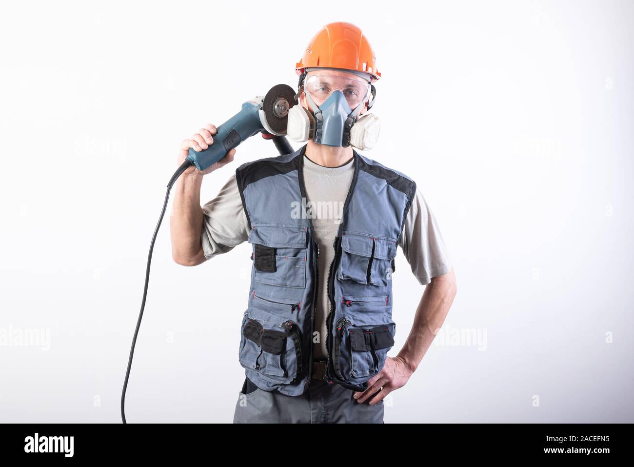 Un builder in un casco e un respiratore, con una smerigliatrice angolare sulla sua spalla. Foto Stock