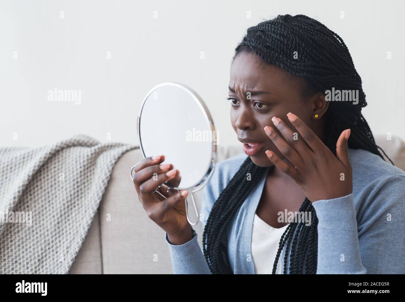Deluso afro donna cercando di specchio e di toccare la sua pelle Foto Stock